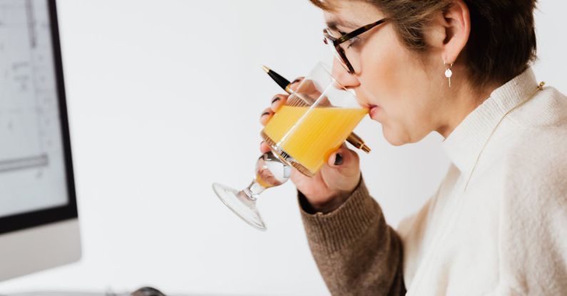 Nutrition Plans - Focused female drinking refreshing juice while working at table in office