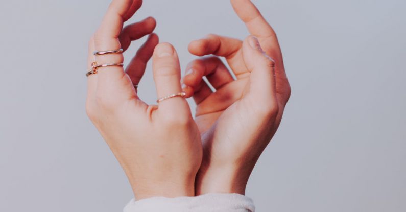 Injuries - Crop faceless female with stylish rings on fingers and hands tied with white bandage against gray background